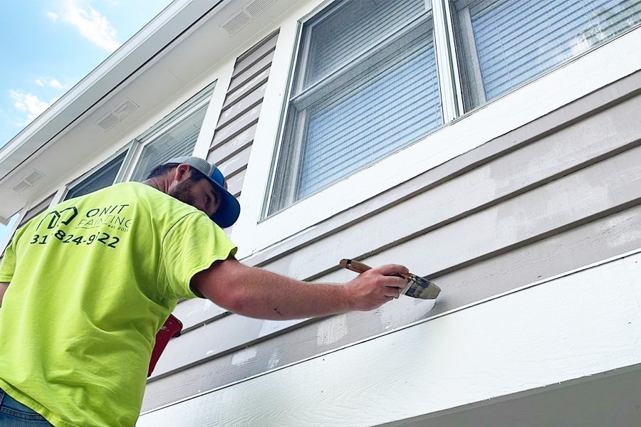 Onit painter painting the siding of a light gray residential home